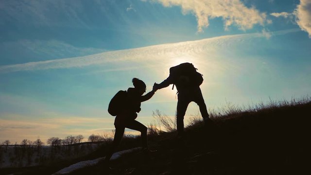 Couple hiking help each other silhouette in mountains. Teamwork couple hiking, help each other, trust assistance, sunset. Man giving hand a woman to help her to climb the mountain.