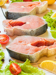 Raw red fish steak with lemon and spices and fresh vegetables on light background.