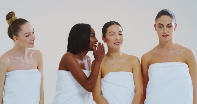 Slow motion of beautiful young smiling women of different ethnicities with perfect firm and slim body in white bathing towels whispering their beauty secrets in the ear and having fun.