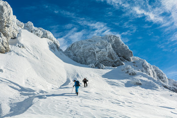 Fototapeta na wymiar Hikers approach the snowy slope under icy rocks.