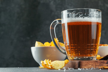 Glass of lager beer with snack bowls on dark stone background