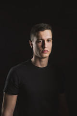 Beautiful, slender young man in black t-shirt on black background and on the street