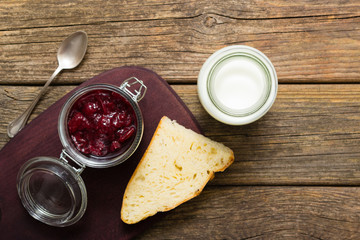breakfast, cherry jam, spoon, milk bottle, slice of bread, old wood table