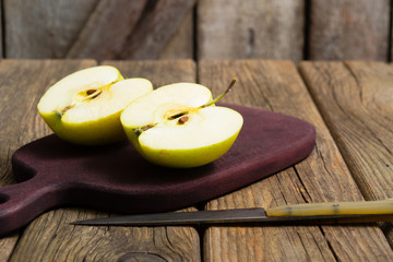 half cut green apples on chopping board, knife, old wooden table