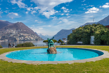 Switzerland - March 10, 2019: A fountain by Lake Lugano with a beautiful statue in the middle of blue water in Ticino canton of Switzerland