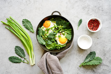 Green shakshusha in frying pan with kale, peas and onions. Top view, gray concrete background