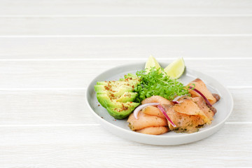 Avocado and smoked salmon on plate. Healthy breakfast. White wooden background
