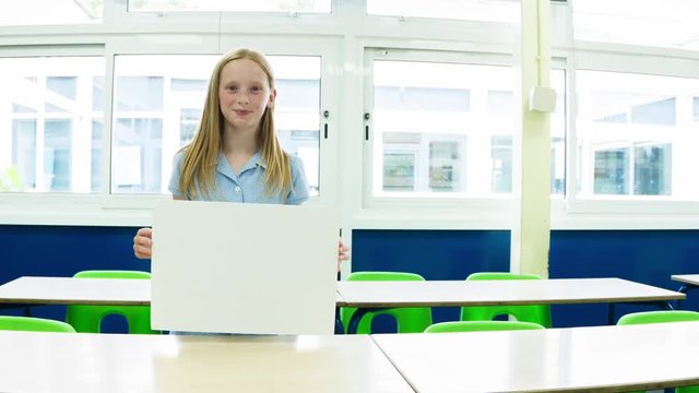 Caucasian primary school girl holding up a blank placard in her classroom themes of copy space placard advertisement