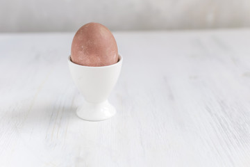 Naturally dyed easter egg for breakfast, white egg cup, white wooden table - minimal easter concept