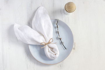 Easter table setting idea, minimal decoration - bunny napkin, coloured egg in white egg cup, willow banch, white wooden table
