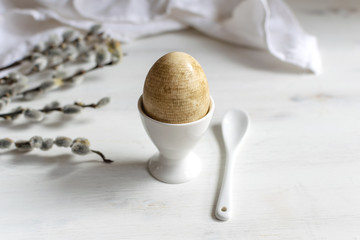 Fototapeta premium Naturally dyed easter egg for breakfast, white egg cup, draped napkin, white wooden table, willow banch - minimal easter concept
