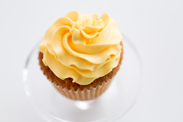 food, pastry and sweets concept - cupcake with yellow buttercream frosting on glass confectionery stand over white background
