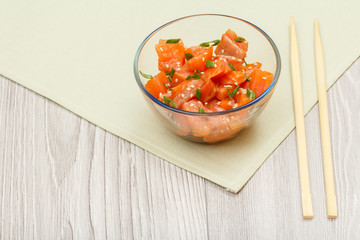 Hawaiian salmon poke with green onions and sesame seeds in glass bowl.