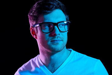 people concept - portrait of young man in glasses and t-shirt over ultra violet neon lights in dark...