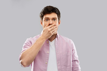 emotion, expression and people concept - shocked and speechless young man covering his mouth by...