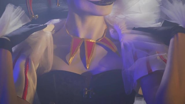Close up of a young woman with clown makeup sitting in the light and touching the collar of her dress