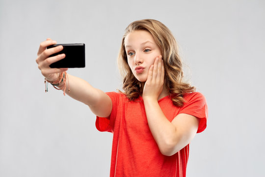 technology and people concept - smiling young woman or teenage girl in red t-shirt taking selfie by smartphone and making duck face over grey background