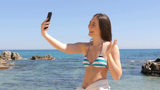 Happy woman in bikini taking selfie with smart phone on the beach on summer vacation