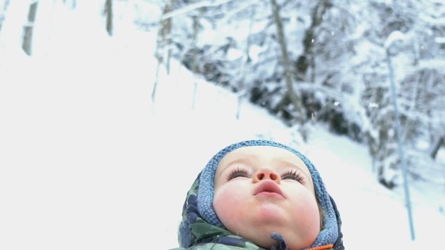 Portrait of little boy with snow on his head looking to sky, slow motion
