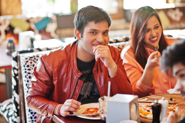 Group of asian friends eating pizza during party at pizzeria. Happy indian people having fun together, eating italian food and sitting on couch.