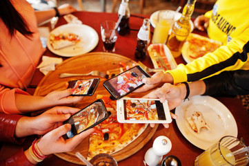 Hands of friends making photo by phones of pizza during party at pizzeria. Happy people having fun...