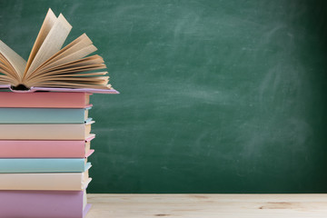 Education and reading concept - group of colorful books on the wooden table in the classroom, blackboard background