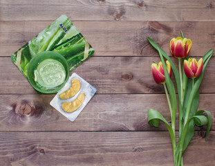 Flatlay Spring Easter bouquet of tulip flowers with cosmetic products, patches on wooden background.View with copy space.