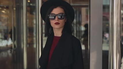 Stylish fashion woman in hat open door and exits from mall