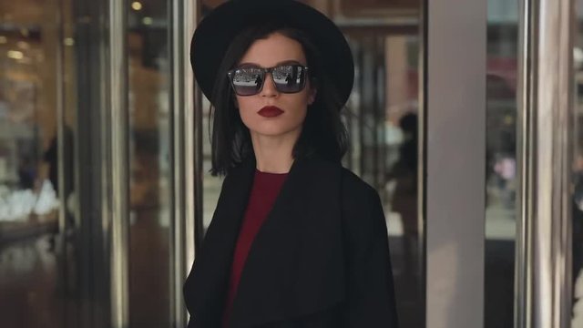 Stylish fashion woman in hat open door and exits from mall