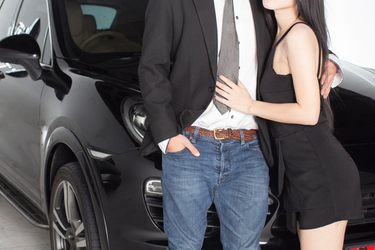 Couple hugging holding each other in front of black luxurious car