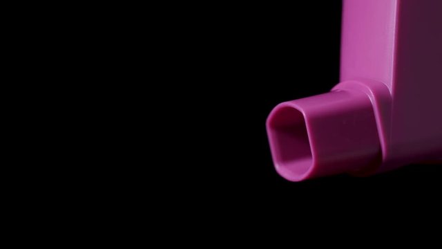 Pink asthma inhaler with spray coming out on black background. Slow motion 50%.