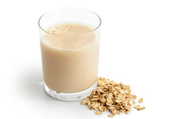 Glass of oat drink  next to a pile of dry oats isolated on white.