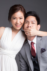 Bride cover her groom's mouth, studio portrait of wedding couple