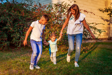 Fototapeta premium Happy family spending time outdoors walking in park. Mother and her son holding little toddler girl. Mother's day