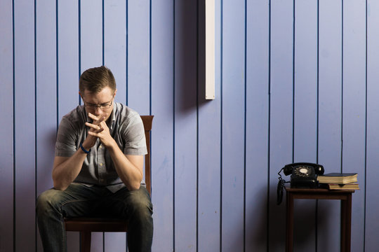 Stressful looking man sitting in room with blue pastel wall