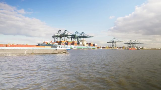 View from vessel looking up river at passing barge and container port in the background in Antwerp, Belgium