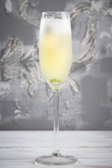 Glass of a cold sparkling wine cocktail drink with olive, on grey background.