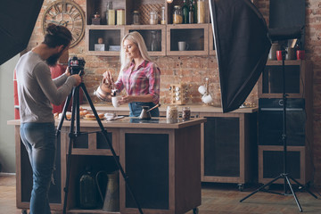 Lifestyle photographer at work. Man shooting young female at loft kitchen. Tea and pastries. Backstage photography.
