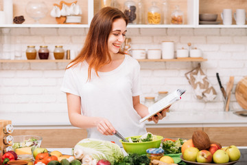 Healthy weight loss and nutritional balance. Woman lifestyle. Young female preparing green salad. Recipe book in hands.