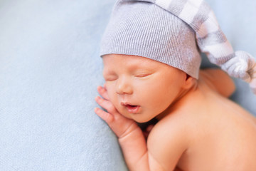 Sleeping newborn baby on the blue background. Child in a nightcap close-up portrait - obrazy, fototapety, plakaty