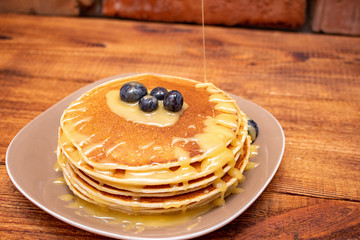 Pancakes with blueberries and honey on the dark brown wooden background