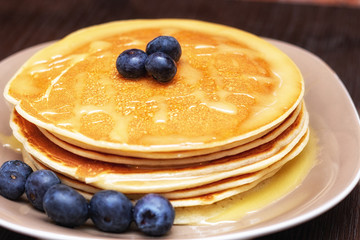 Pancakes with blueberries and honey on the dark brown wooden background