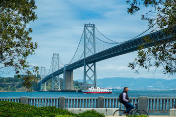 San Francisco Bay bridge with blurry man riding bicycle during day time