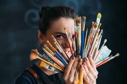 Artist and art supplies. Tools for talent. Smiling woman painter in apron posing with paintbrushes bunch.