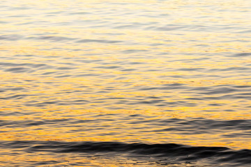small wave and water ripple background in orange evening sunset light and fog rising in the distance