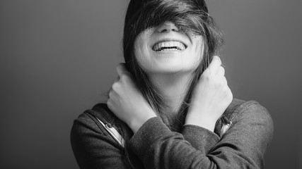 Cheerful mood. Young woman covering eyes with hair. Toothy smile. Black and white portrait. Copy space.