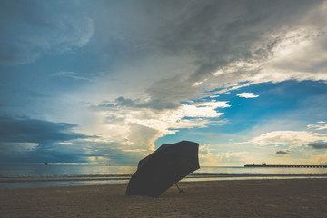 Umbrella left on dark beach with cloud covering up the sky before storm. Conceptual image of preparation for coming problem