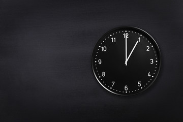 Black wall clock showing one o'clock on black chalkboard background. Office clock showing 1am or 1pm on black texture