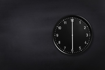 Black wall clock showing six o'clock on black chalkboard background. Office clock showing 6am or 6pm on black texture