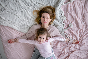 Beautiful young mother and her little daughter are lying together on the bed in the bedroom,...